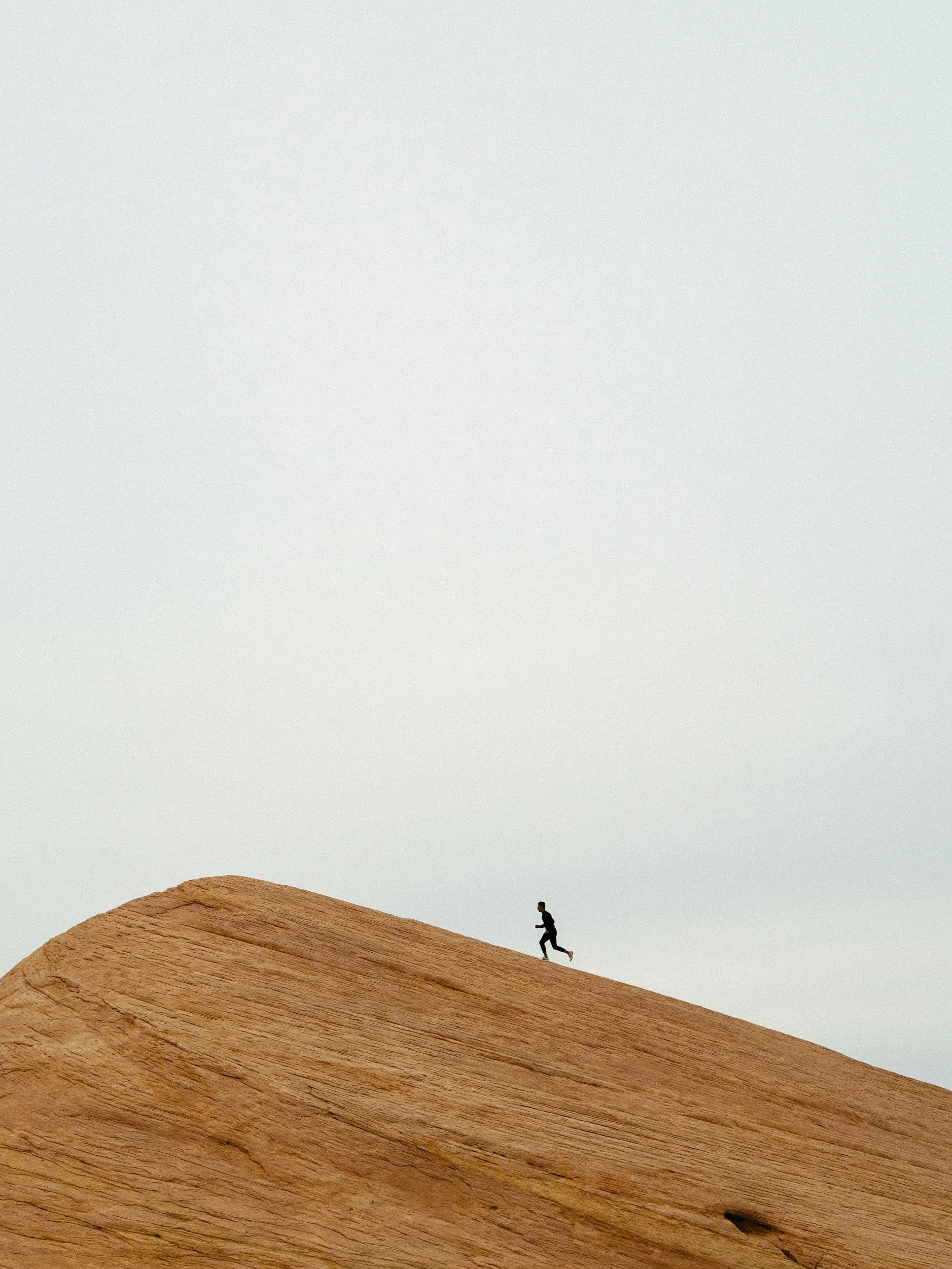 A lone runner cresting a sunlit dune ridge.