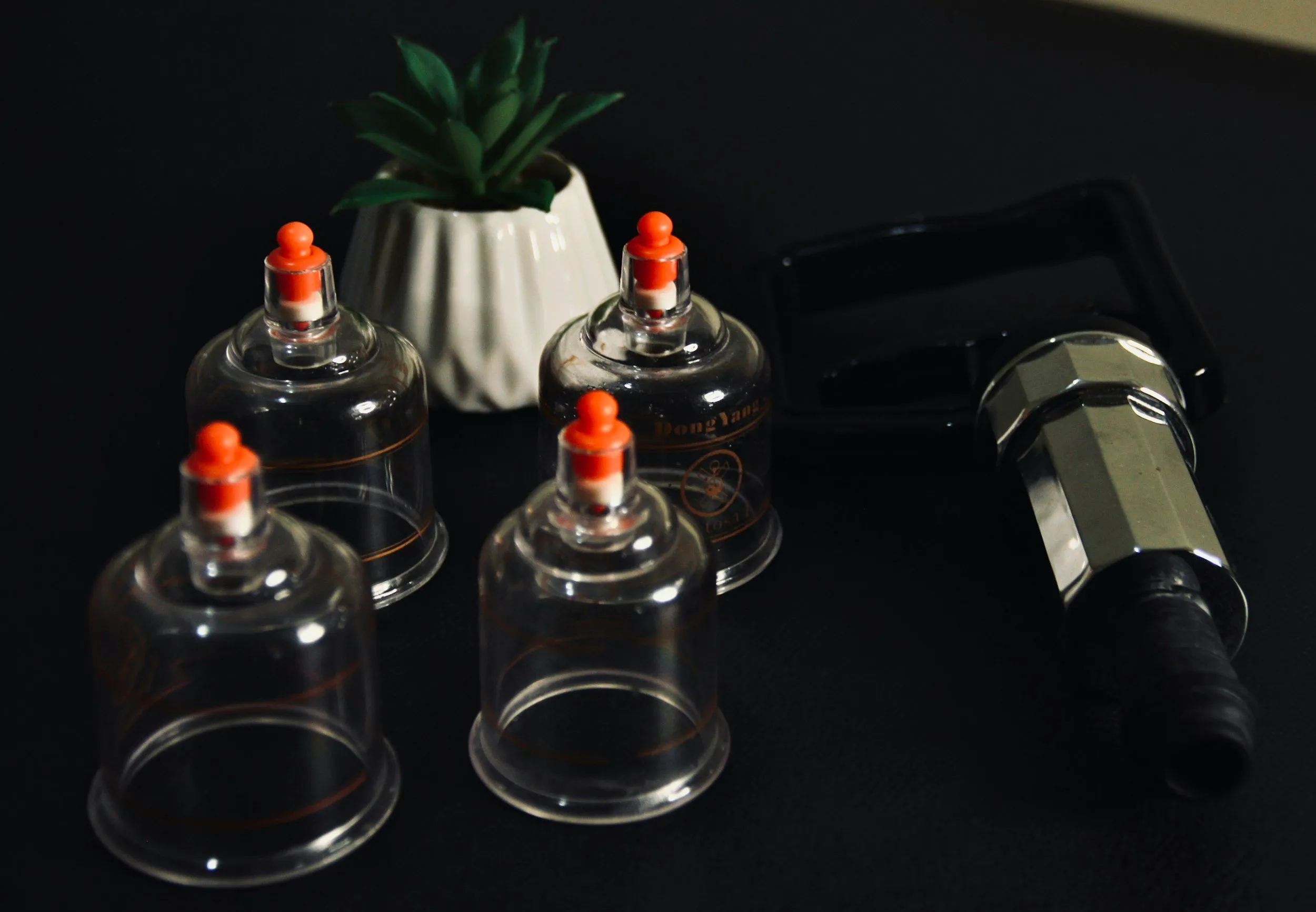 A set of glass cupping vessels and a suction pump on a dark surface.